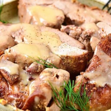 Sliced roasted pork with gravy and dill garnish on a plate.