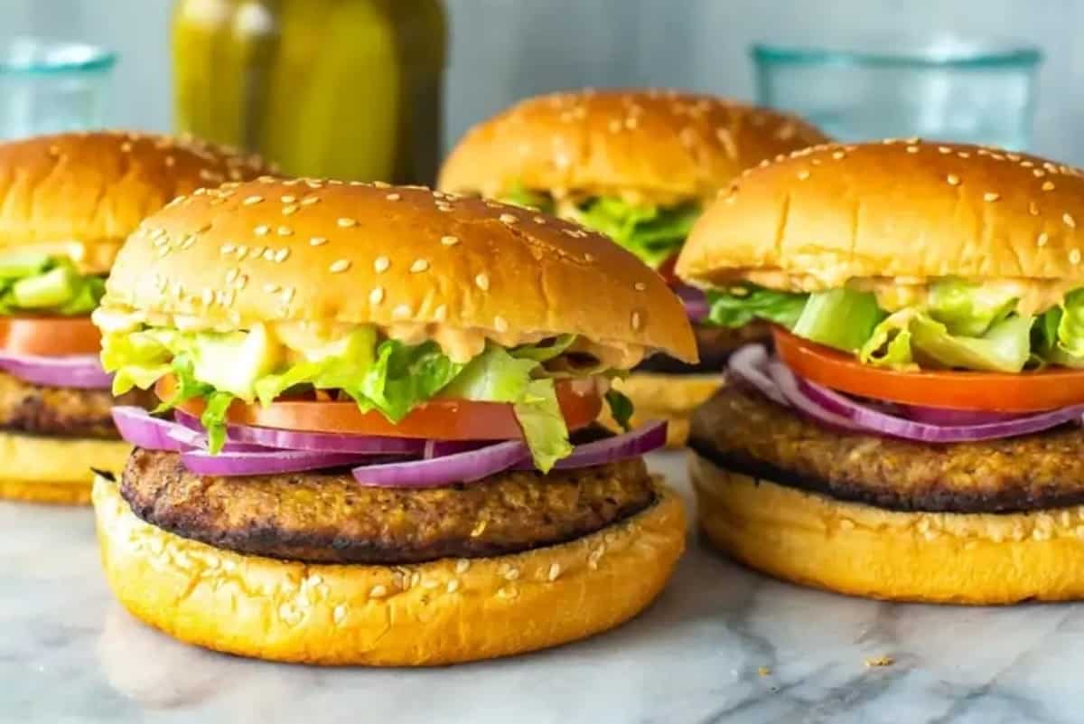 Three classic burgers with lettuce, tomato, onion, and beef patties on sesame seed buns.