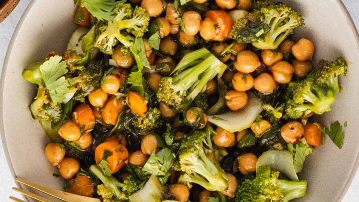 A bowl containing roasted chickpeas and broccoli with a garnish of herbs.