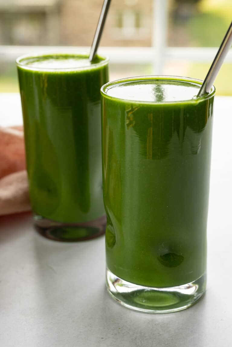 Two glasses of green smoothie using Vitamix recipes sit on a table.