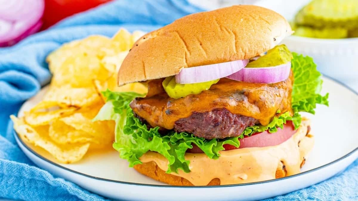 A cheeseburger with lettuce, tomato, pickles, and red onion, served with a side of potato chips.