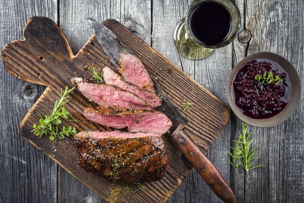 A steak on a wooden cutting board with cranberry sauce and a glass of Vermentino.
