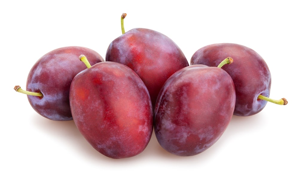 Four plums and vegetables on a white background.