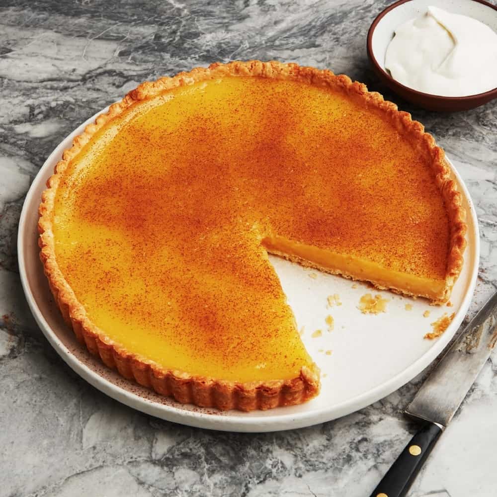 A lemon tart on a plate with vanilla whipped cream.