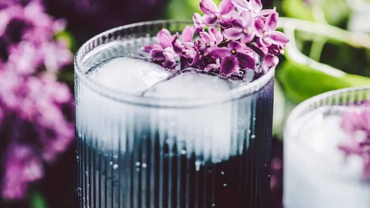 A cocktail with purple flowers and ice in a glass.