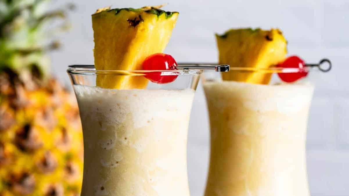 Two pina colada cocktails garnished with pineapple slices and cherries.