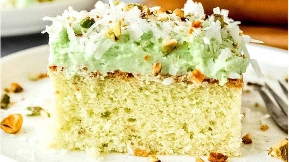 A slice of cake with green frosting and pistachios.