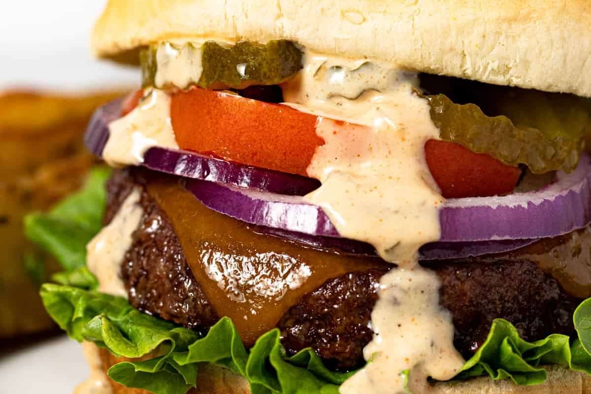 Close-up of a cheeseburger with lettuce, tomato, pickles, onions, and sauce.