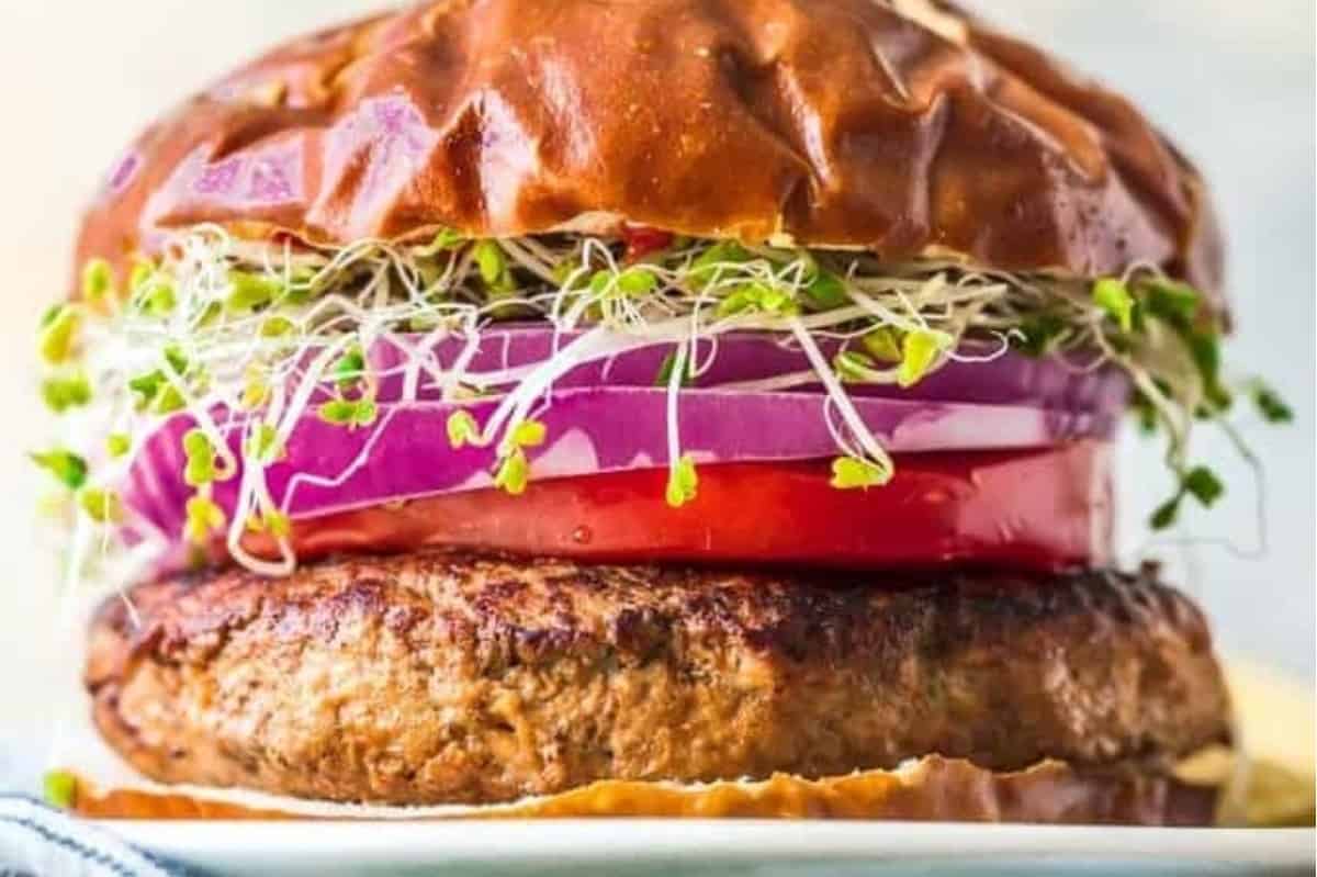 Close-up of a burger with a beef patty, tomato, red onion, and sprouts on a brioche bun.