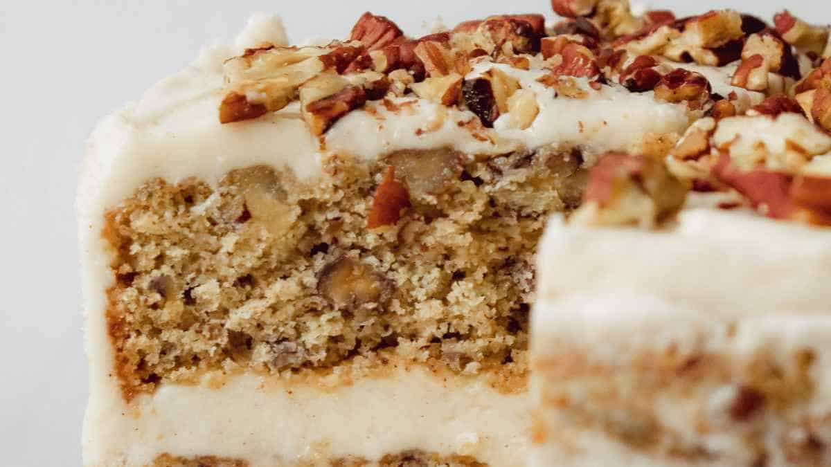 A slice of carrot cake topped with cream cheese frosting and chopped pecans.