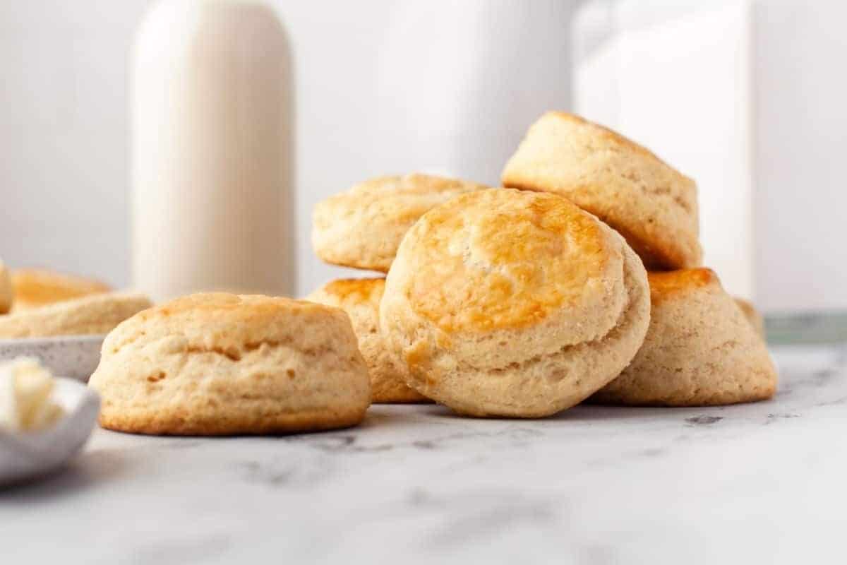 Freshly baked biscuits on a marble countertop with a bottle of milk in the background.