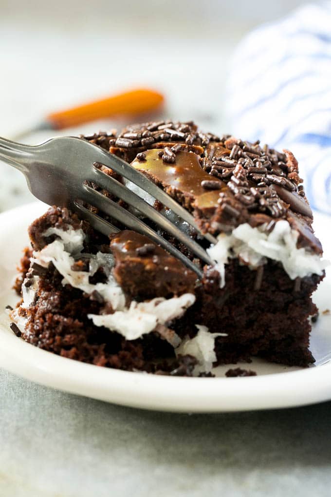 A fork taking a piece of chocolate coconut cake. 
