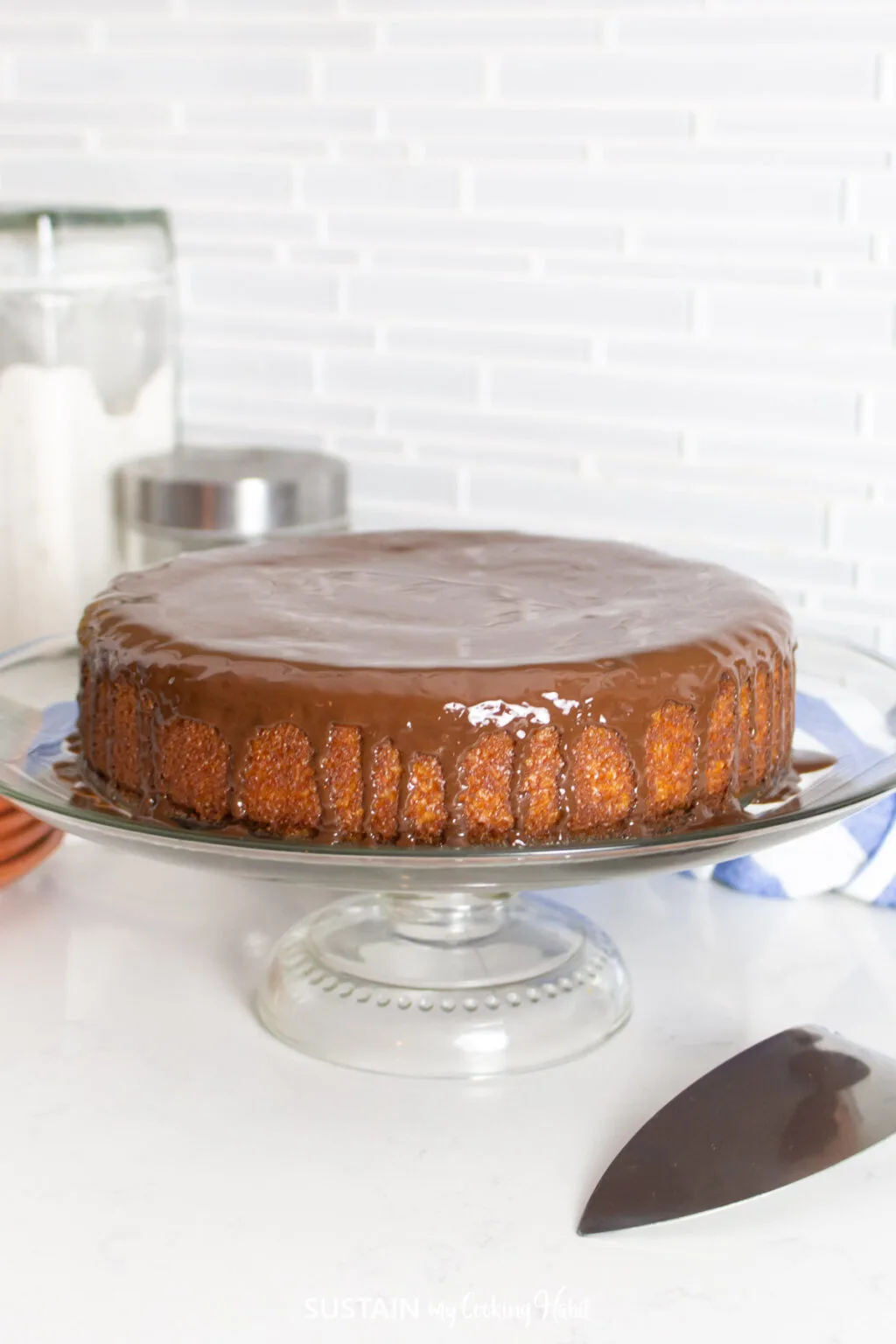 Coconut cake with a chocolate glaze topping placed on a cake stand. 
