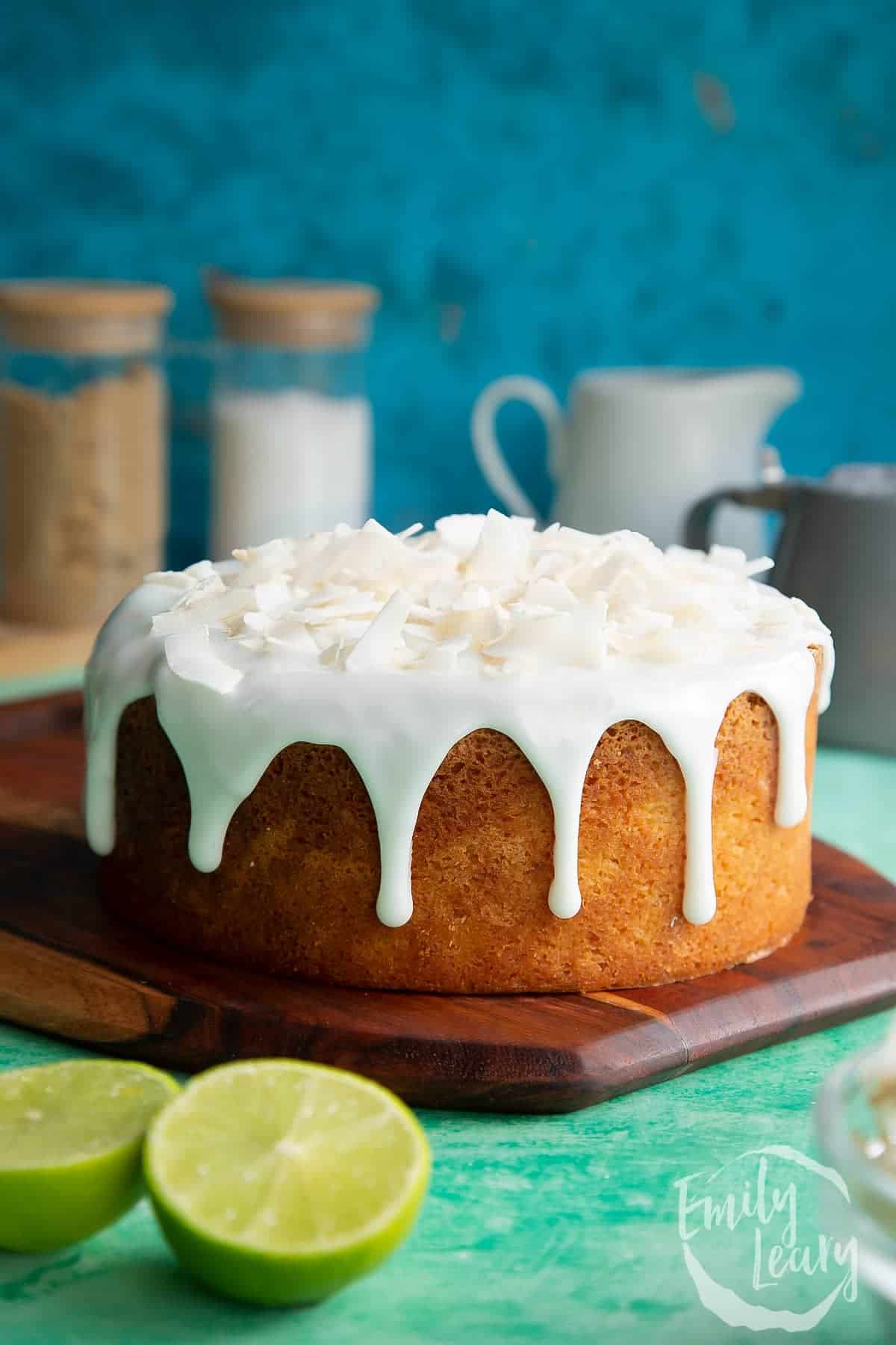A cake with icing and lime slices on a wooden cutting board, perfect for coconut lovers.