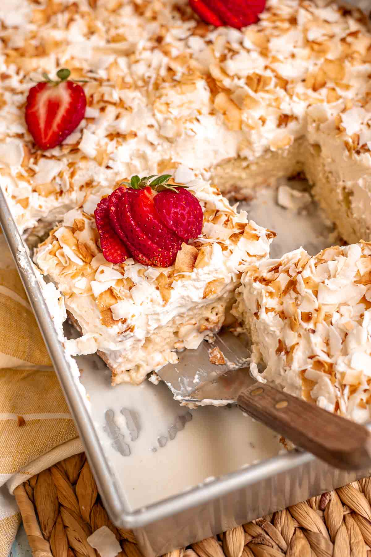A spatula removes a soaked piece of coconut tres leches cake from a pan. 
