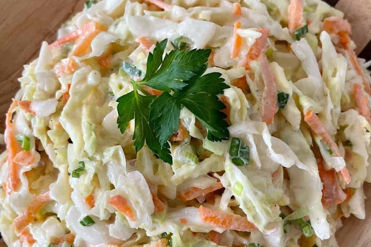 A bowl of creamy coleslaw garnished with a sprig of parsley.