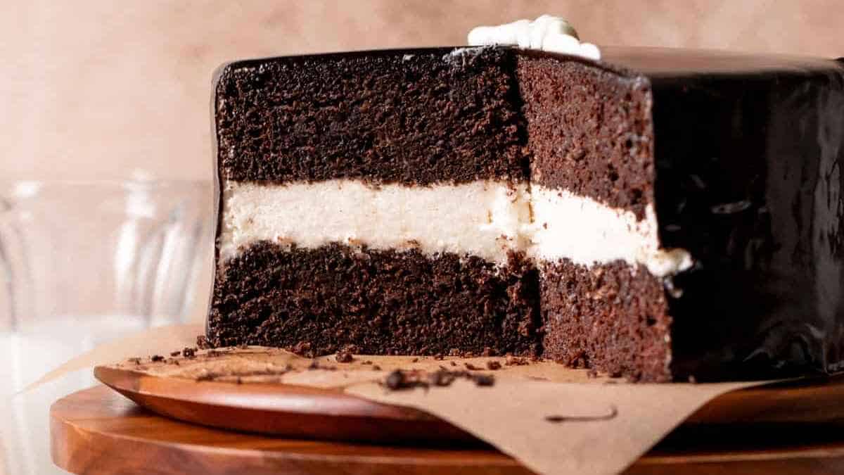 A slice of layered chocolate cake with white cream filling and glossy chocolate ganache.
