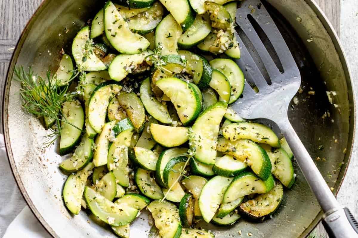 Sautéed zucchini slices with herbs in a frying pan.