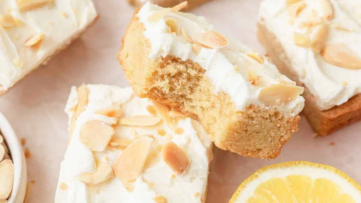 Slices of almond and lemon cake with white frosting and sliced almonds on top.