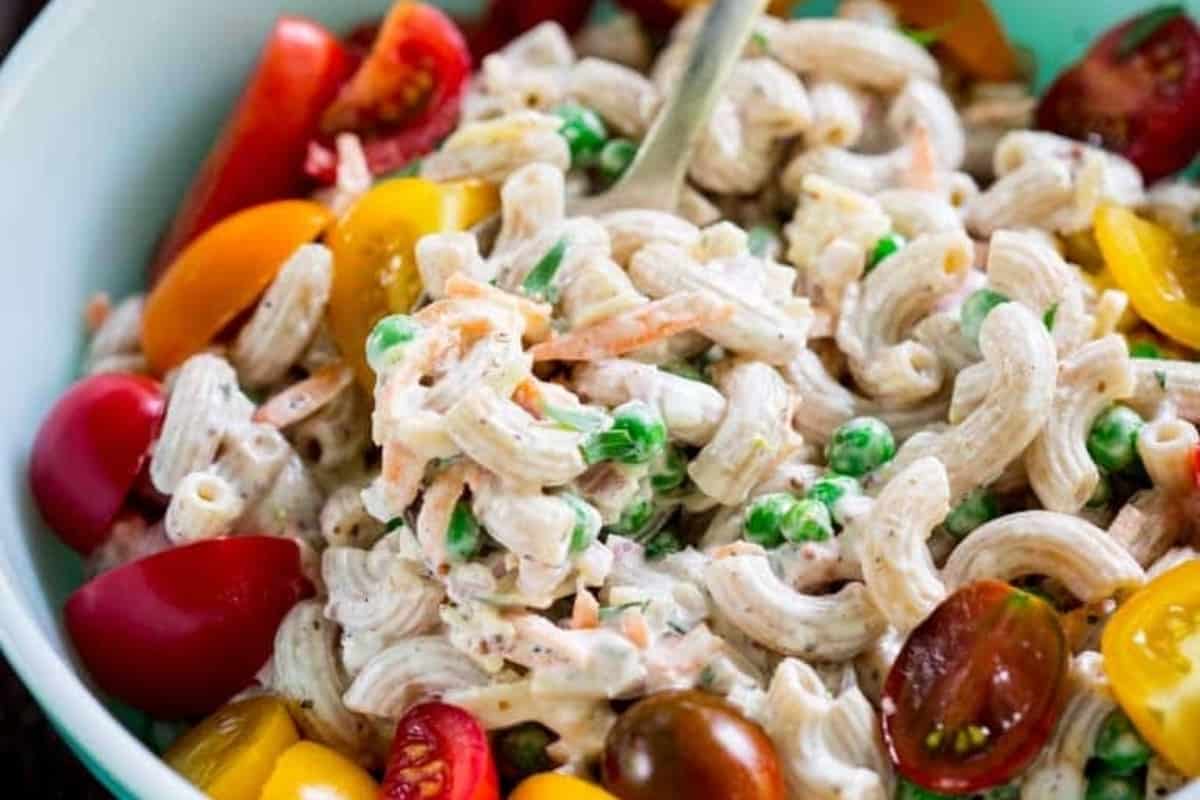 A bowl of pasta salad with tomatoes and peas.