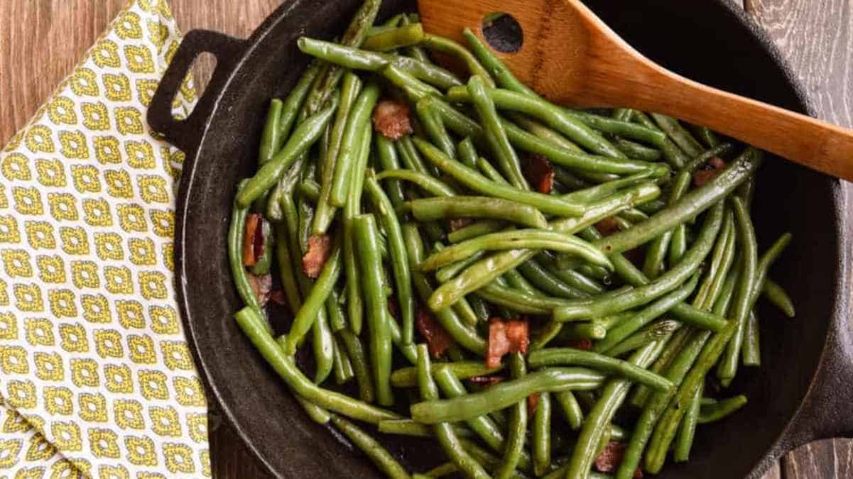 Sautéed green beans with bacon pieces in a cast iron skillet.