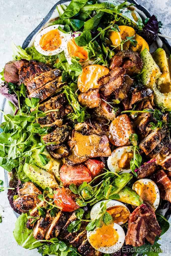 A platter filled with grilled chicken cobb salad with bacon vinaigrette poured over the top.
