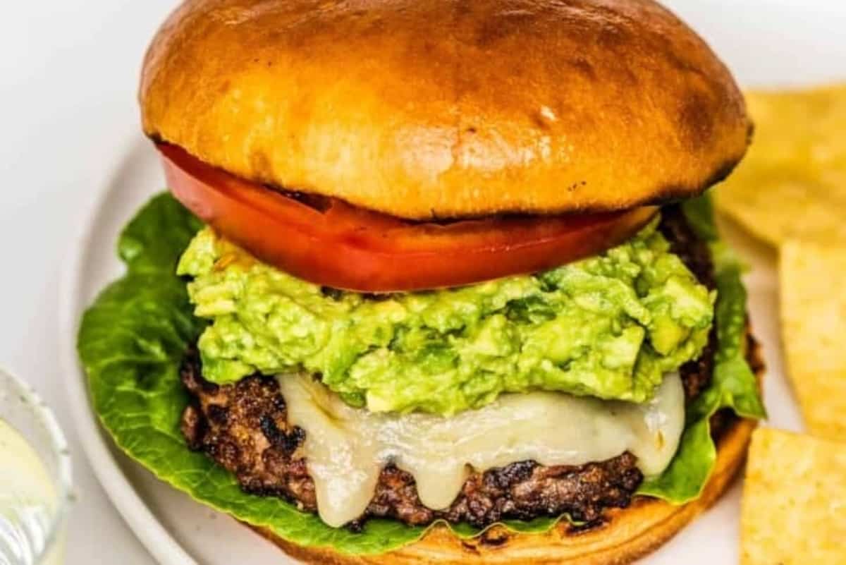 Beef burger with melted cheese, guacamole, lettuce, and tomato, served with tortilla chips.