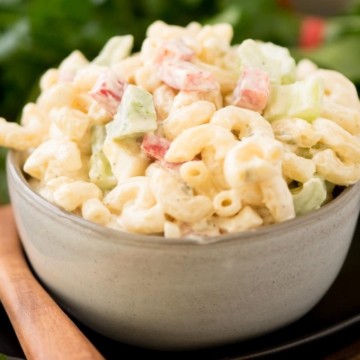 A bowl of creamy macaroni salad with diced vegetables on a wooden table.