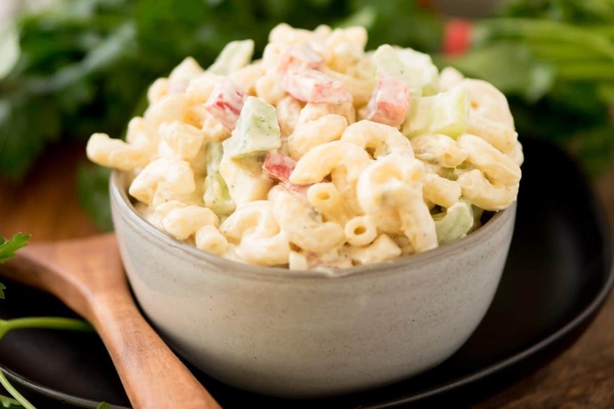 A bowl of creamy macaroni salad with diced vegetables on a wooden table.