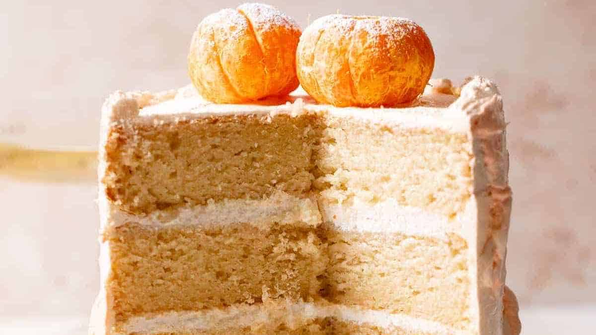 A slice of layered vanilla cake with frosting, topped with two small round pastries.