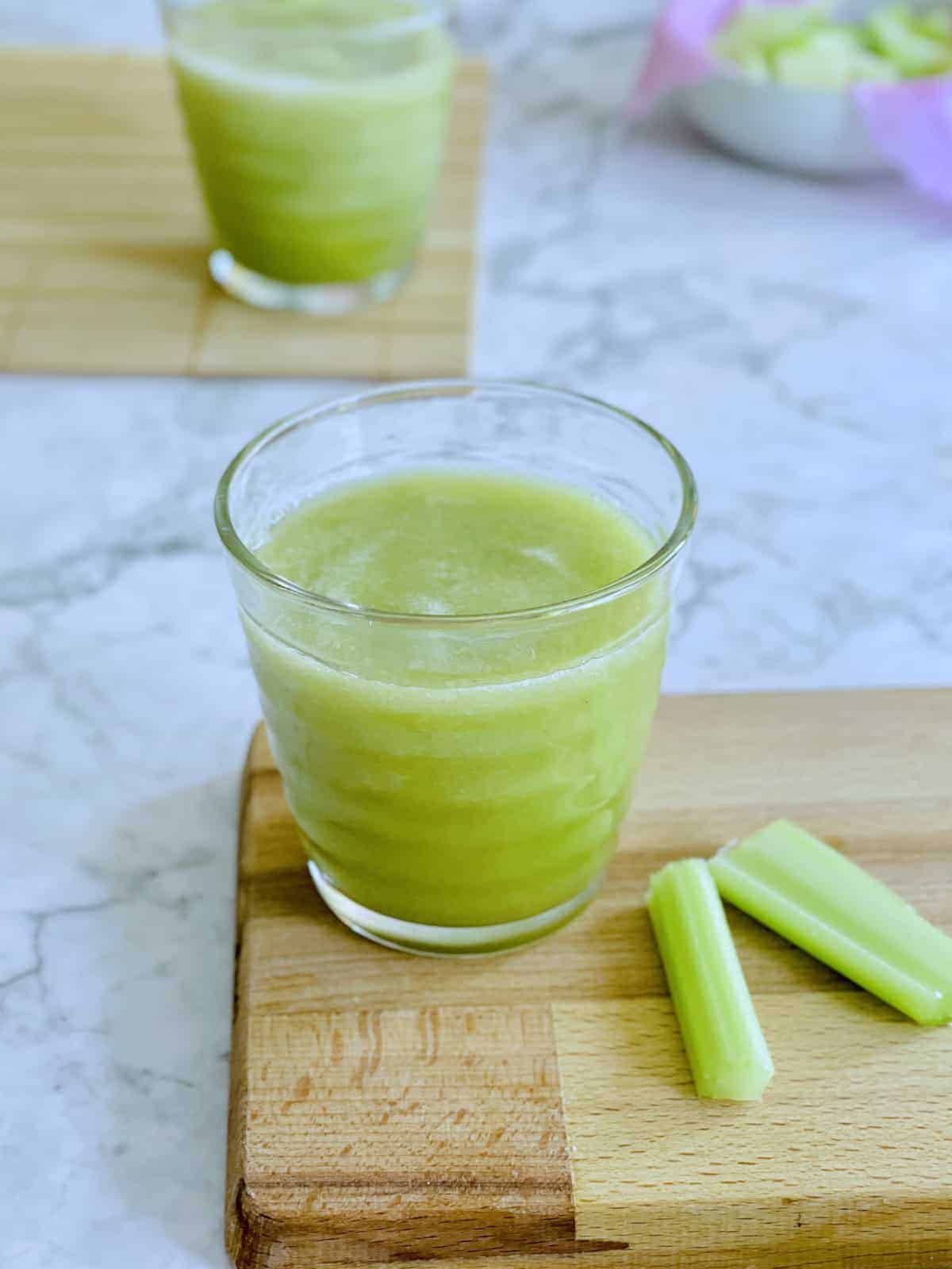 organic celery juice served in glass on board with celery sticks on the side. 
