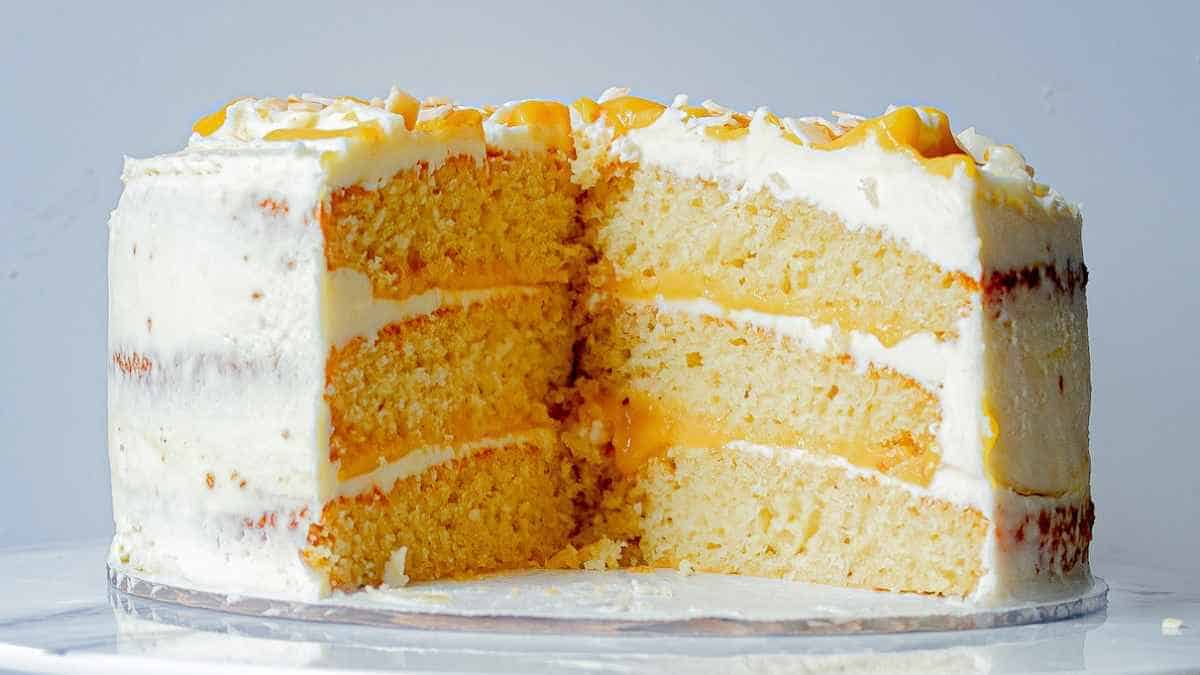 A three-layered vanilla cake with white frosting and caramel drizzle, with a slice removed to show the interior.