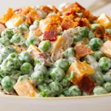Pea salad in a white bowl with bacon and peas.