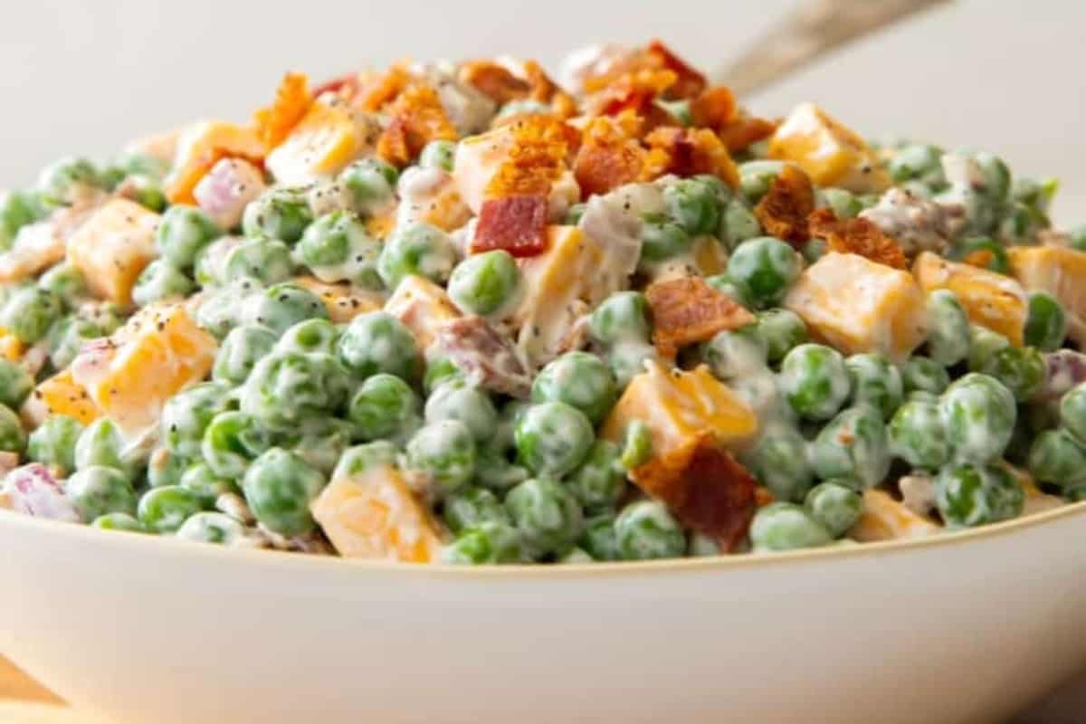 Pea salad in a white bowl with bacon and peas.