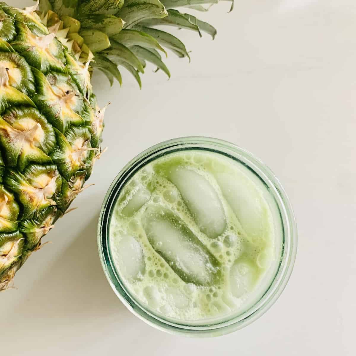 A glass of ice-cold pineapple juice with a fresh pineapple garnish, perfect for summer refreshment.