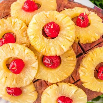 Glazed ham topped with pineapple rings and cherries on a serving platter.