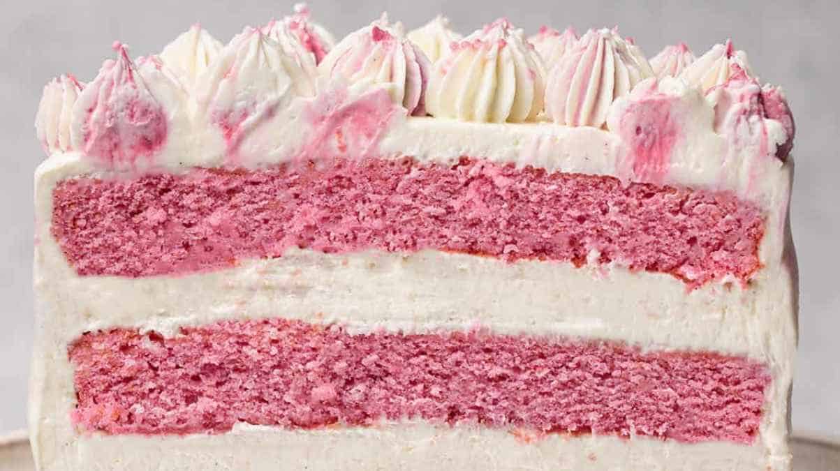 Layered strawberry cake with white frosting and decorative piping.