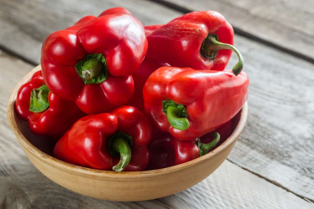 Red peppers in a wooden bowl on a rustic table.