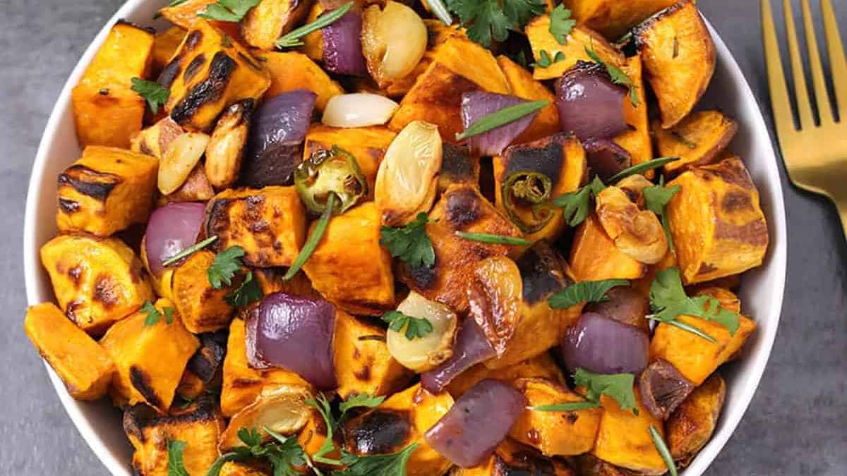 A bowl of roasted sweet potatoes with onions and herbs.