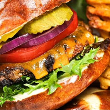 Close-up of a cheeseburger with lettuce, tomato, pickles, onions, and a side of french fries.
