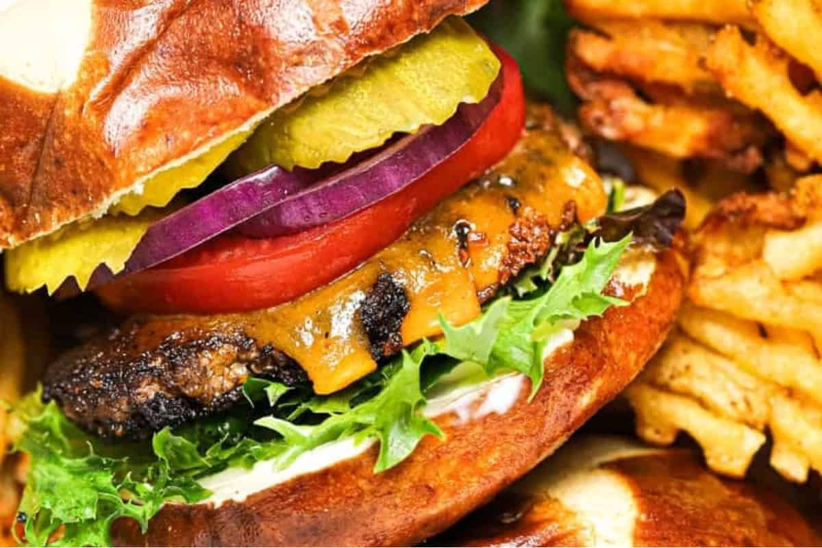 Close-up of a cheeseburger with lettuce, tomato, pickles, onions, and a side of french fries.