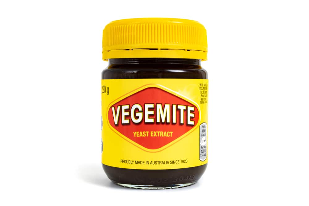 A jar of vegemite and vanilla beans on a white background.