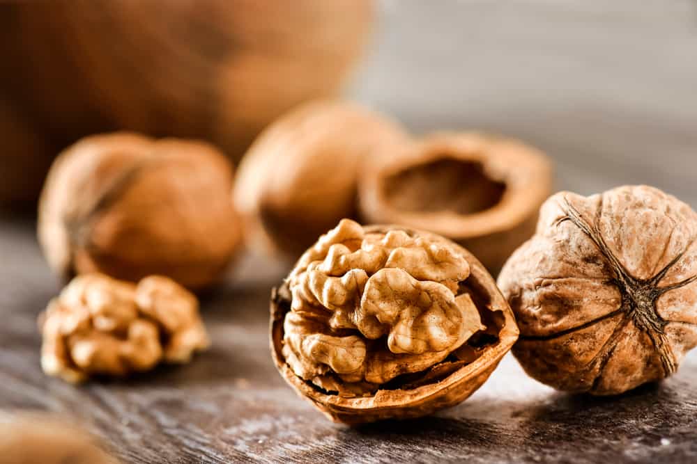 Walnuts, both whole and cracked open, on a wooden surface, depict wholesome foods that start with W.