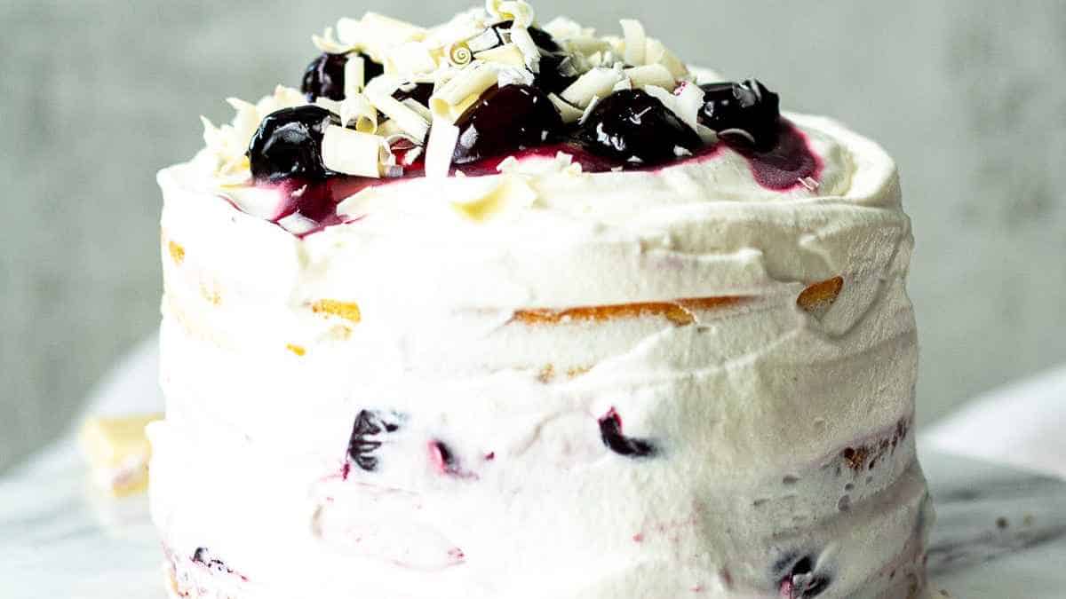 Layered berry cake with white frosting and topped with chopped nuts and fruit garnish.