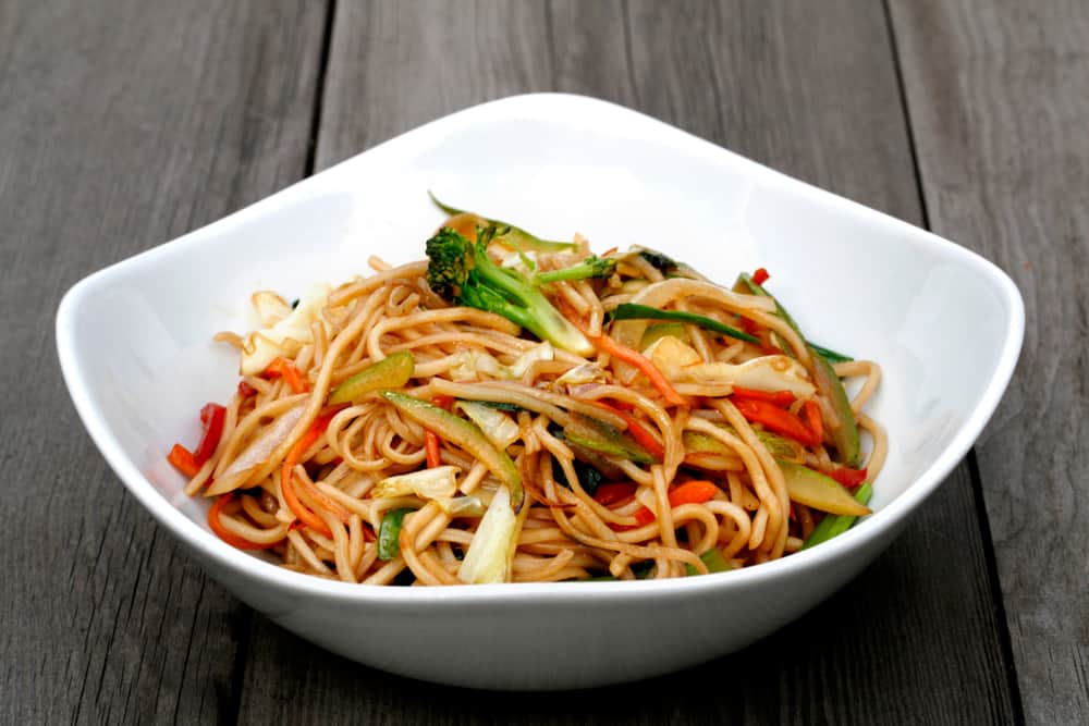 A bowl of stir-fried noodles with mixed vegetables and yams.