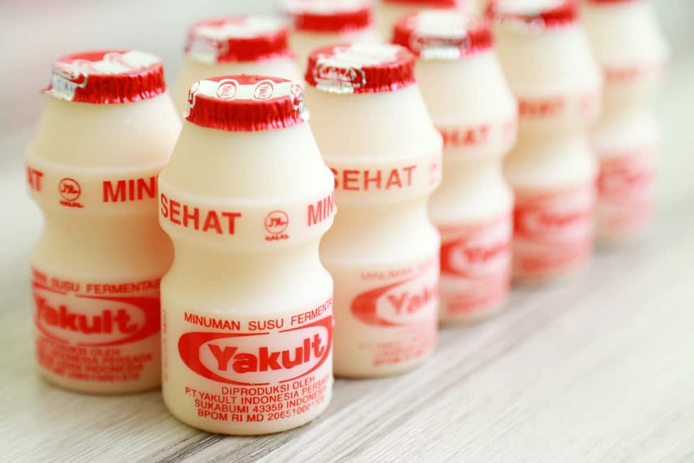 Small bottles of yakult probiotic milk beverage arranged on a table alongside yams.