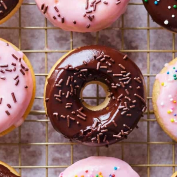 Assorted frosted doughnuts with sprinkles, displayed on a wire cooling rack.