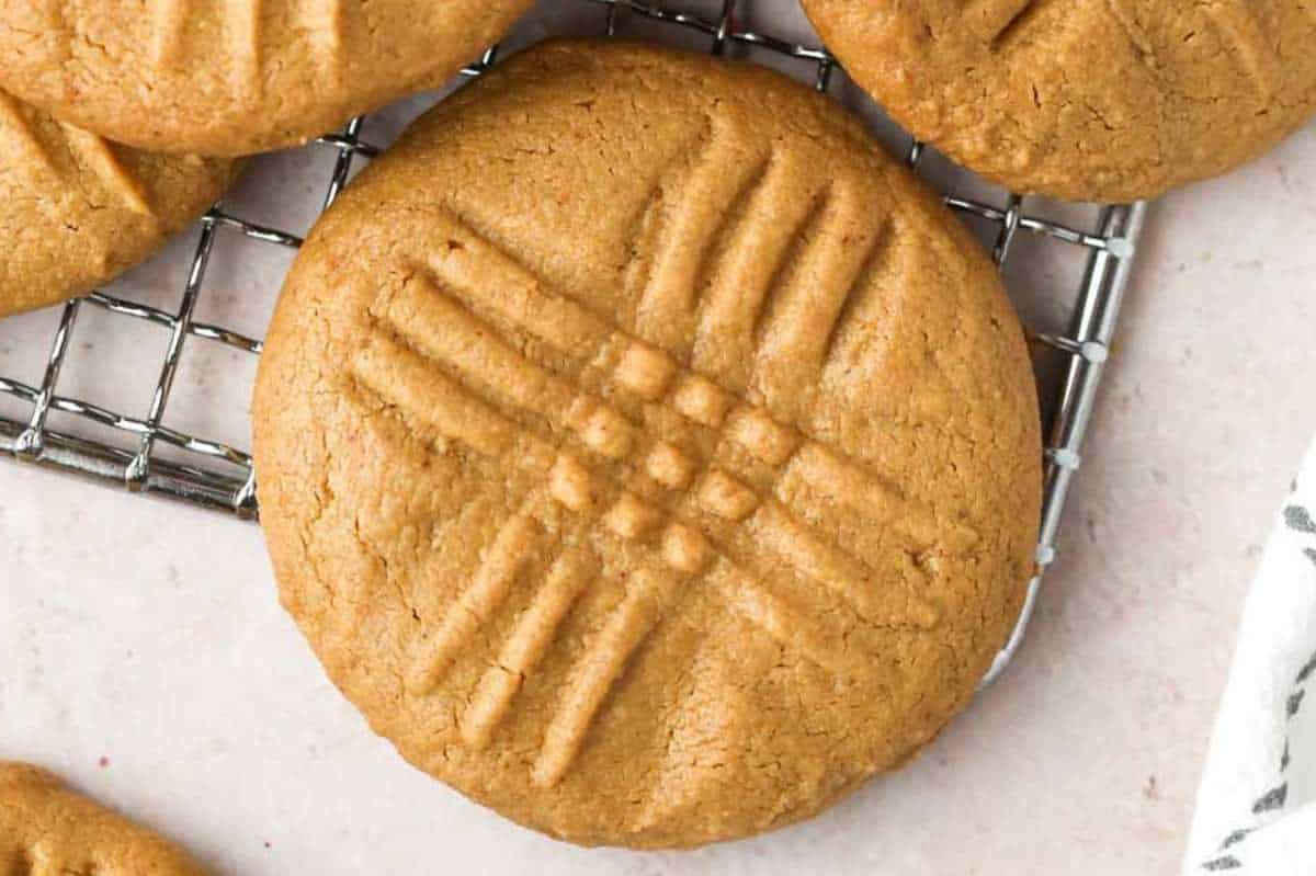 Golden-brown peanut butter cookies with criss-cross marks, cooling on a wire rack.