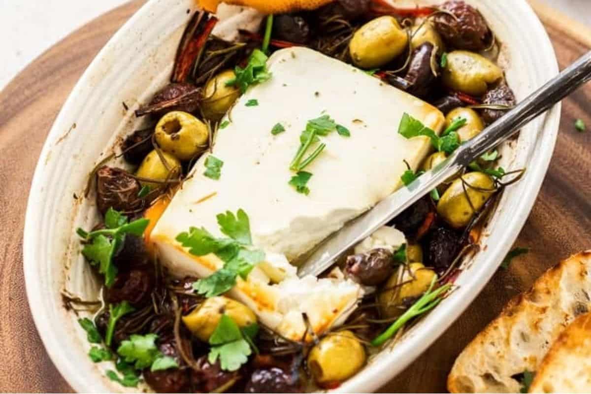 A block of feta cheese baked with olives and herbs, served with crusty bread.