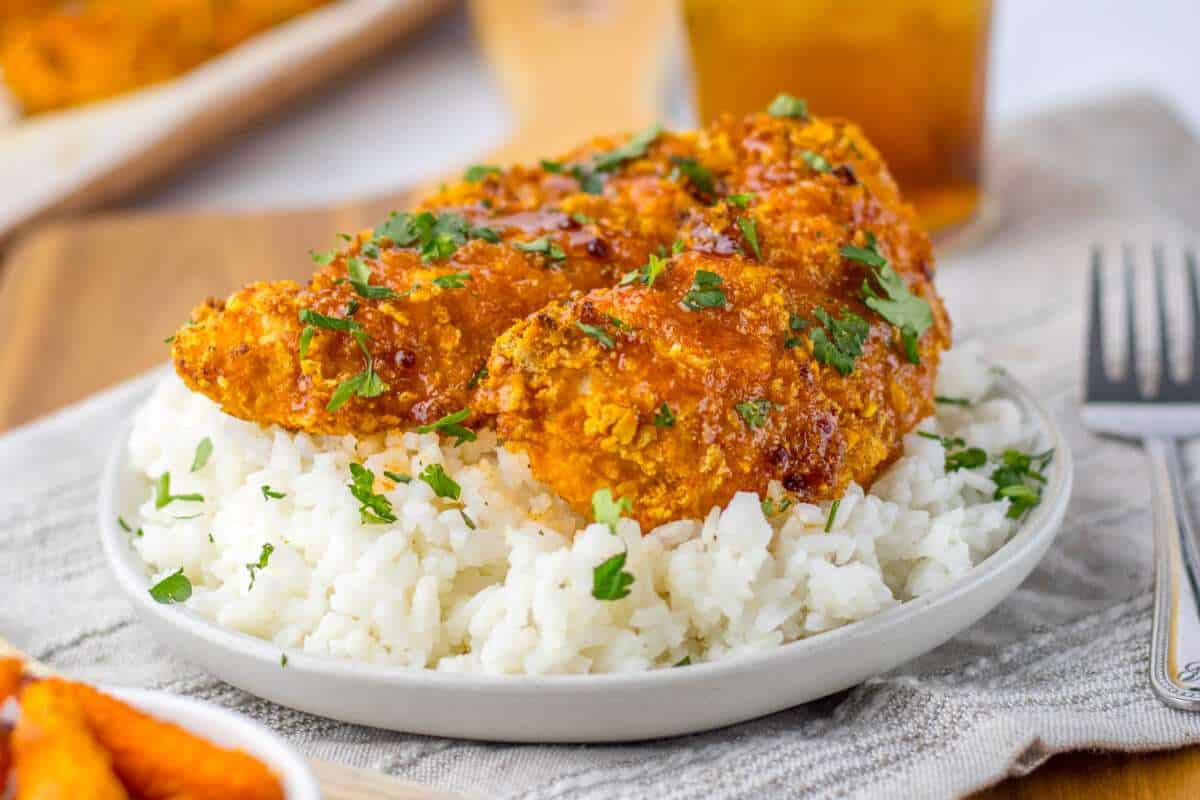 A bowl of white rice topped with crispy fried chicken garnished with fresh parsley, served on a wooden table.